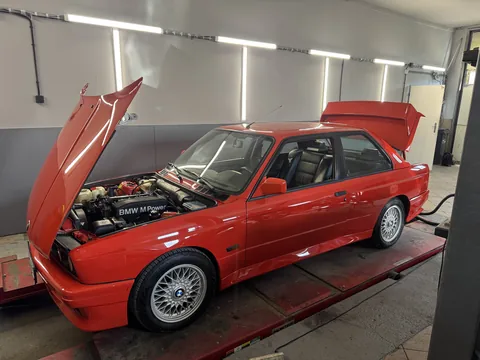 Červené BMW E30 při servisu v dílně.