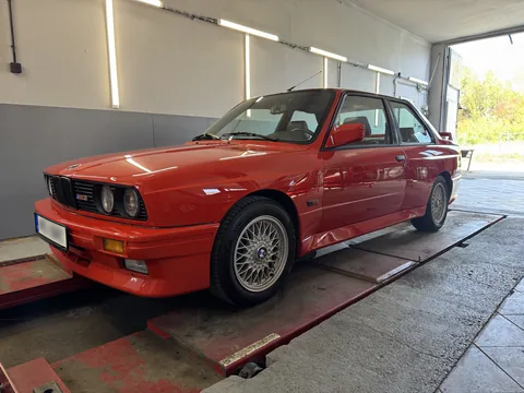 Červené BMW E30 v dílně při pohledu zepředu.