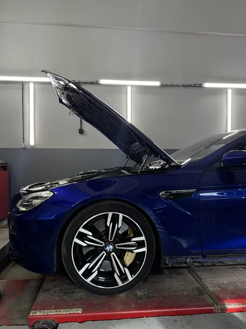 Modré BMW s otevřenou kapotou na servisní plošině.