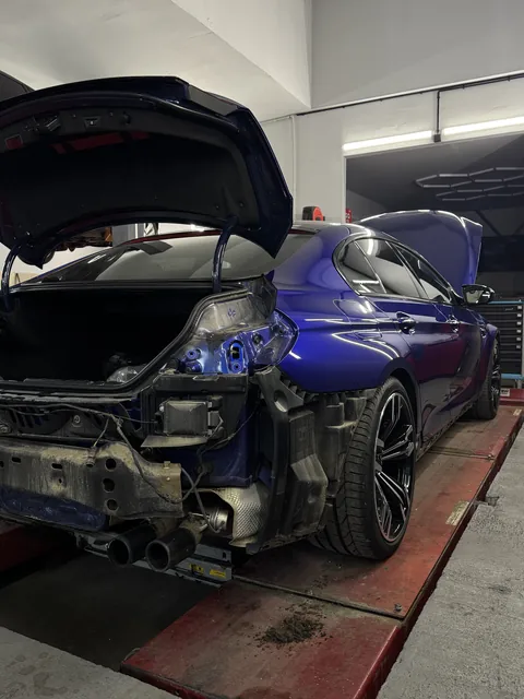 Modré BMW při opravě zadní části s demontovaným nárazníkem.
