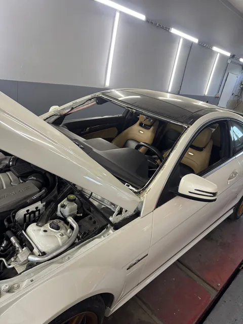 Bílý Mercedes s otevřenou kapotou při opravě.